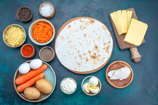 Top view fresh vegetables with cheese and seasonings on dark blue background.