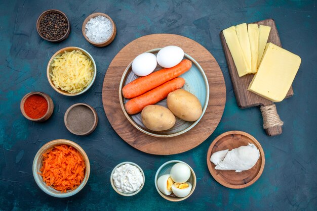 Top view fresh vegetables with cheese and seasonings on the dark-blue desk.