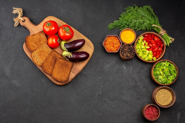 Top view fresh vegetables with dark bread loafs and seasonings on the dark surface salad meal bread food