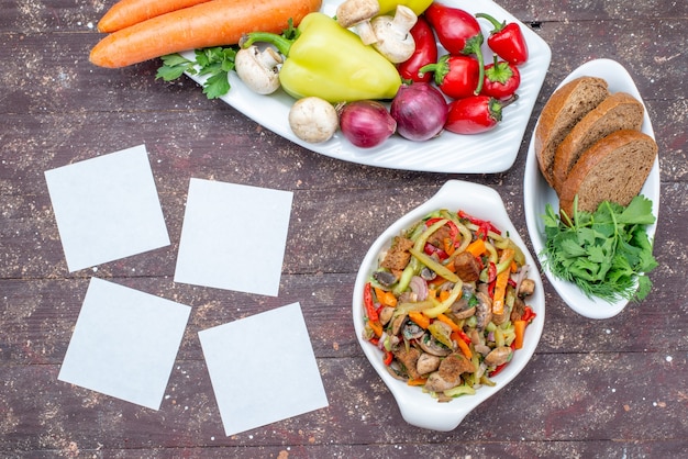 Top view of fresh vegetables with mushrooms inside plate with bread loafs and greens on brown, vegetable food meal mushroom