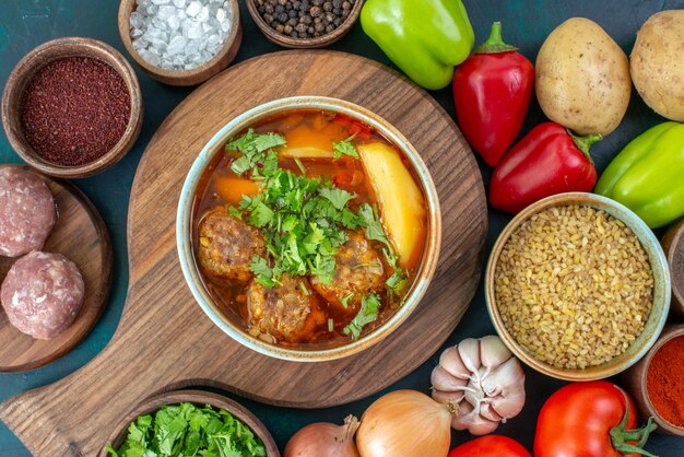 Top view fresh vegetables with seasonings meat soup and greens on the dark blue desk