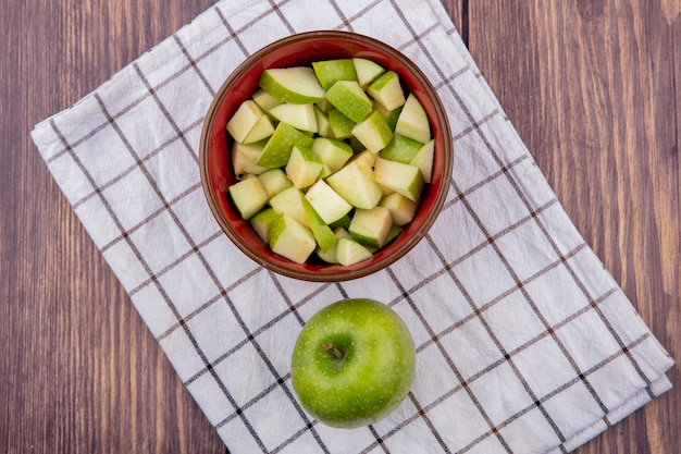 Top view of fresh whole apple with chopped apple slices on red bowl on checked tablecloth and wood