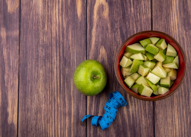 Top view of fresh whole apple with chopped apple slices on red bowl on wood with copy space