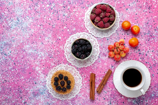 Top view fresh wild berries raspberries and blackberries with little cake and tea on pink desk.