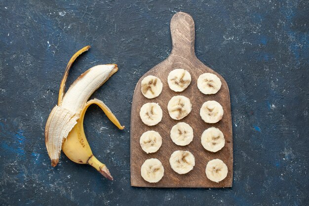 top view of fresh yellow banana sweet and delicious peeled out and sliced on dark-blue desk, fruit berry sweet vitamine health