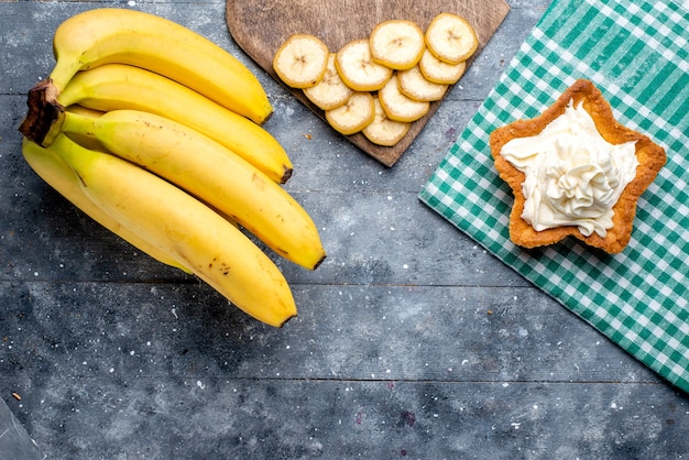 top view of fresh yellow bananas whole berries with cake on grey desk, fruit berry vitamine taste