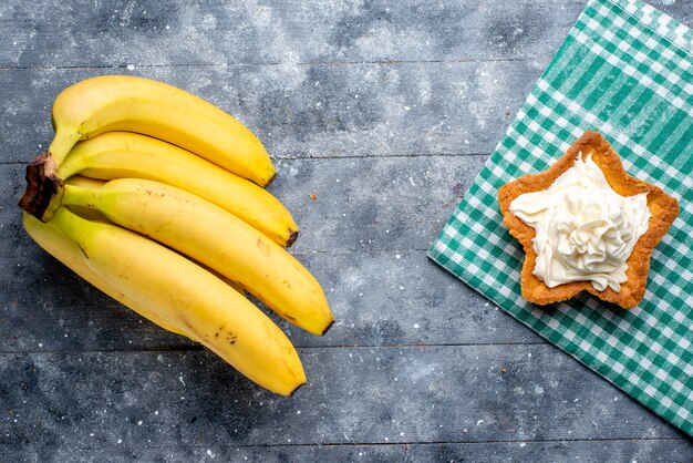 вид сверху свежих желтых бананов целых ягод с пирогом на сером, фруктово-ягодном вкусе витамина