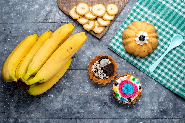 top view of fresh yellow bananas whole berries with cakes on grey, fruit berry vitamine taste