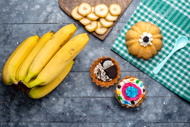 top view of fresh yellow bananas whole berries with cakes on grey, fruit berry vitamine taste