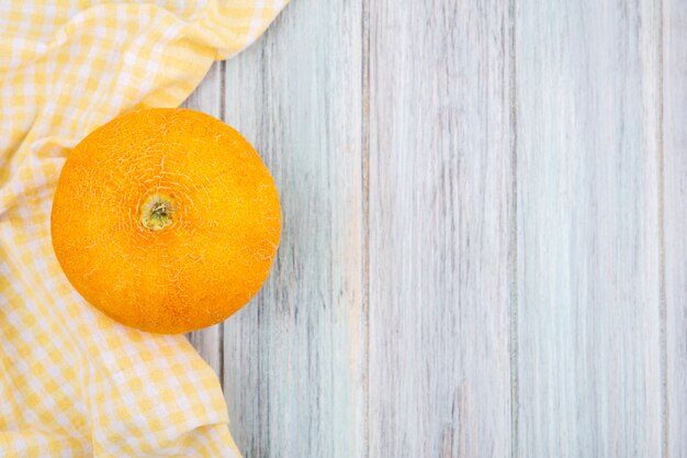 Top view of fresh and yellow cantaloupe melon with yellow checked tablecloth on grey wood with copy space