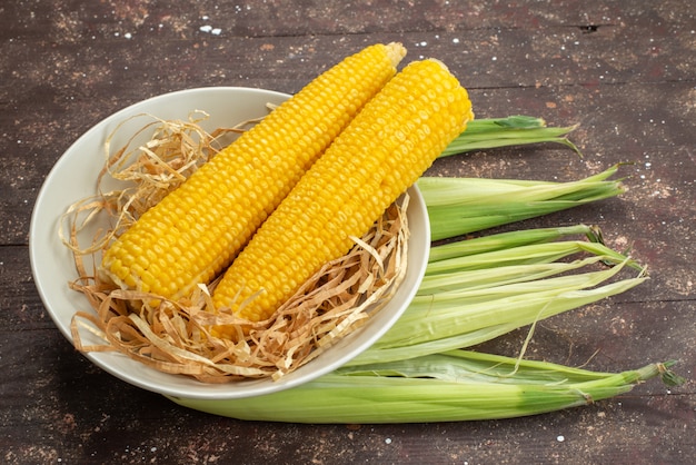 Top view fresh yellow corns inside white plate with peels on brown food