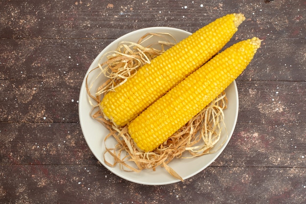 Top view fresh yellow corns inside white plate on wood