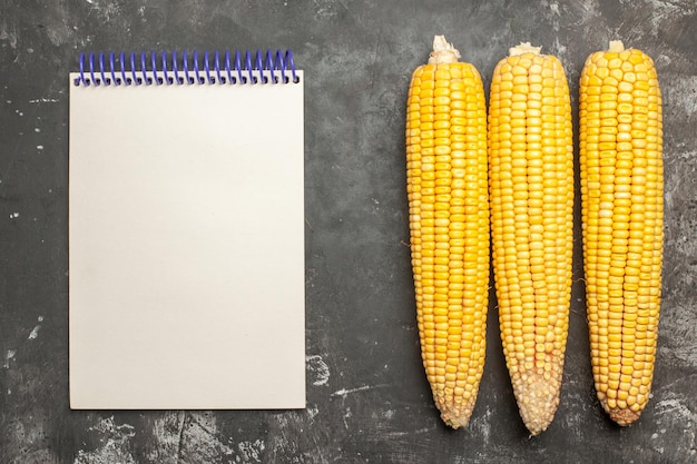 Free photo top view fresh yellow corns with notepad on dark background