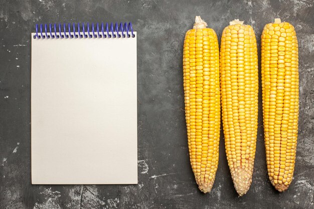 Top view fresh yellow corns with notepad on dark background