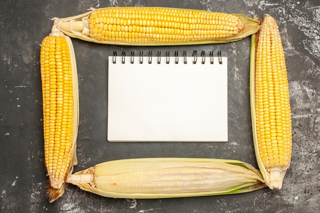 Free photo top view fresh yellow corns with notepad on dark background