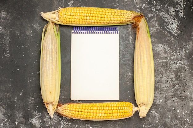 Free photo top view fresh yellow corns with notepad on dark background