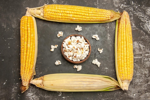 Free photo top view fresh yellow corns with poopcorn on dark background