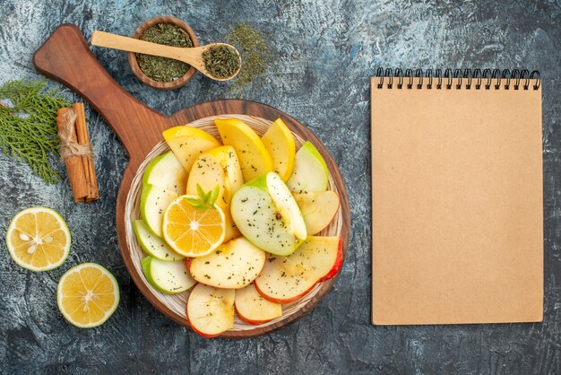 Top view of fresh yellow green red apple slices on a white plate with lemon on a wooden cutting board cinnamon limes on gray background