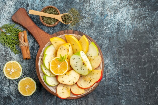 Top view of fresh yellow green red apple slices on a white plate with lemon on a wooden cutting board cinnamon limes on gray background