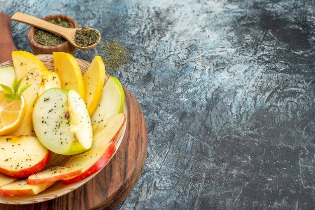 Top view of fresh yellow green red apple slices on a white plate with lemon on a wooden cutting board