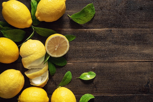 Free photo top view fresh yellow lemon fruits with leaves on wet wood table background with copy space still life photography