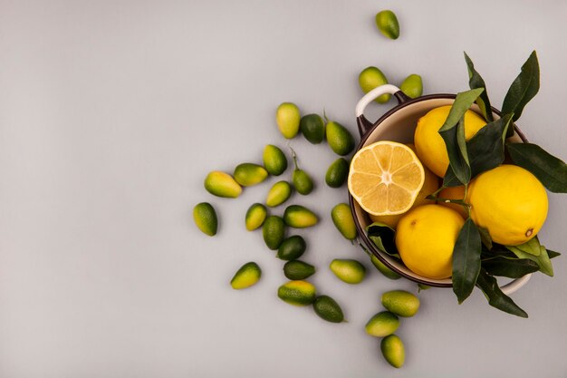 Top view of fresh yellow lemons on a bowl with kinkans isolated on a white wall with copy space