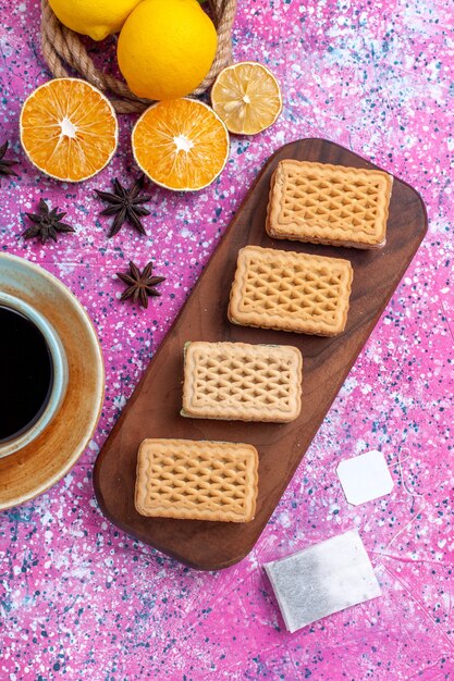 Vista dall'alto limoni gialli freschi frutta acida dolce con biscotti sandwich waffle sulla scrivania rosa.