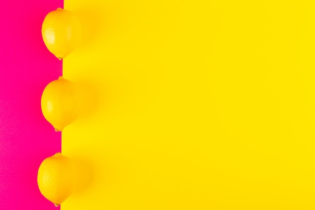 Foto gratuita una vista dall'alto limoni gialli freschi maturi succosi morbidi interi foderati sullo sfondo rosa-giallo frutti agrumi estate