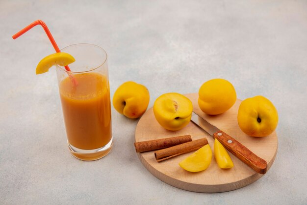 白い背景の上の新鮮な桃ジュースとシナモンスティックのナイフで木製キッチンボード上の新鮮な黄色の桃のトップビュー