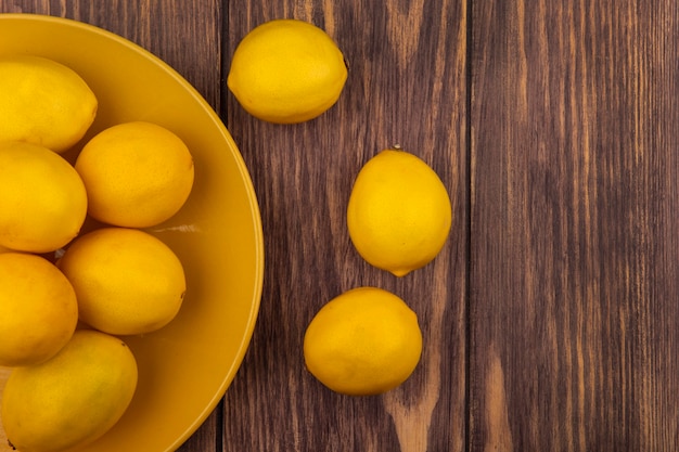 Вид сверху свежих лимонов с желтой кожурой на желтой тарелке на деревянной стене с копией пространства