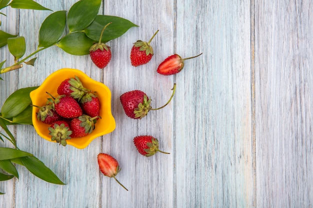 Top view of freshdelicious strawberries on a yellow bowl with strawberries isolated on a grey wooden background with copy space