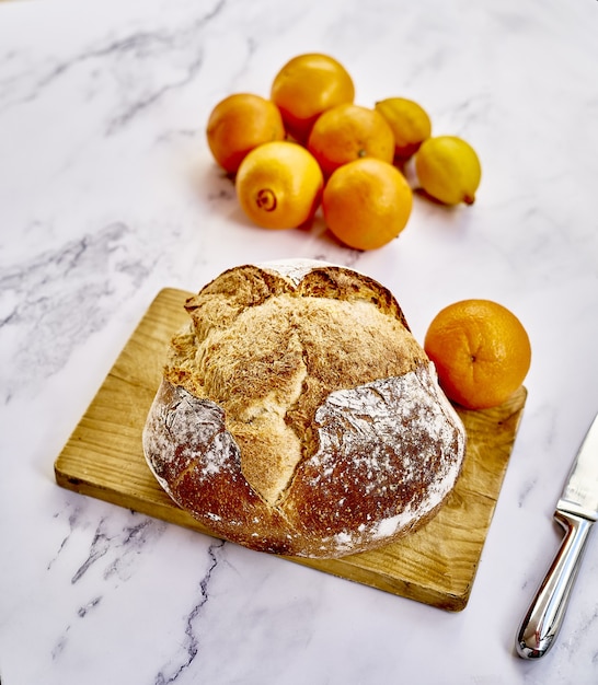 Вид сверху на свежеиспеченный традиционный хлеб с апельсинами, лимонами и ножом