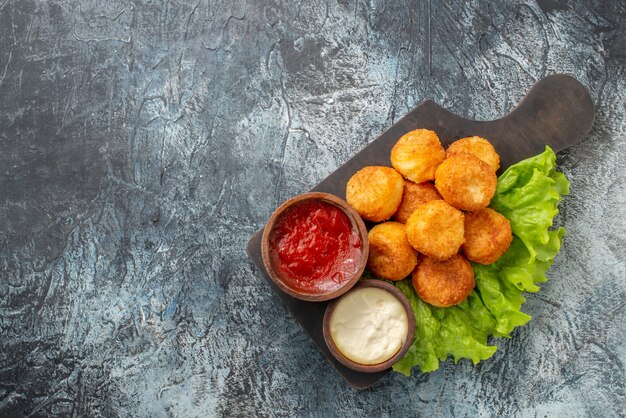 Top view fried cheese balls lettuce sauce bowls on chopping board on grey table free space