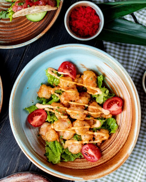 Top view of fried chicken with tomatoes and sauce on lettuce on a plate on rustic