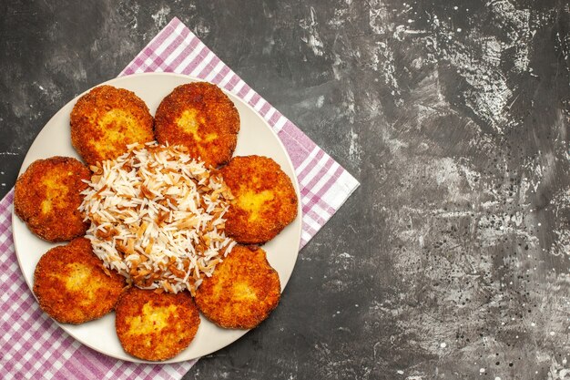 Top view fried cutlets with cooked rice on the dark surface meat food dish rissole