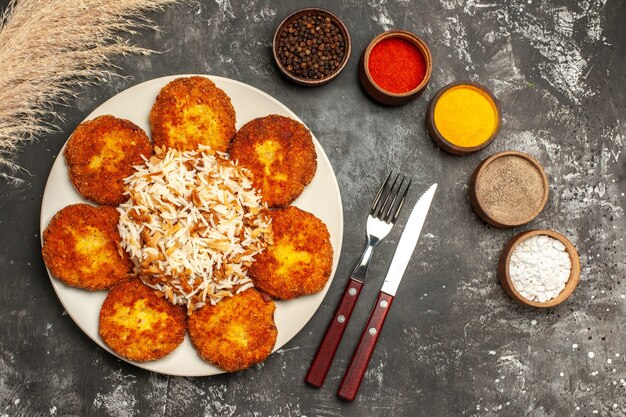 Foto gratuita vista dall'alto cotolette fritte con riso cotto e condimenti sul piatto di carne di cibo foto piano scuro