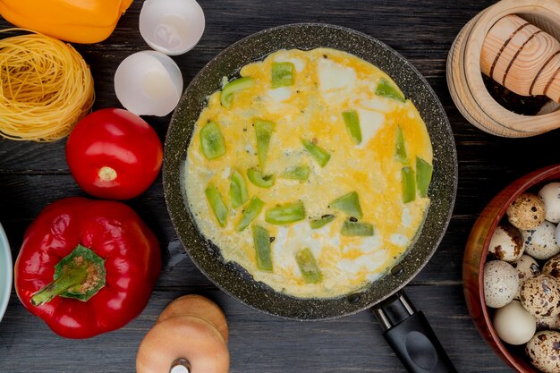 Top view of fried egg on a frying pan with chopped slices of green pepper with quail eggs on a wooden bowl on a wooden background