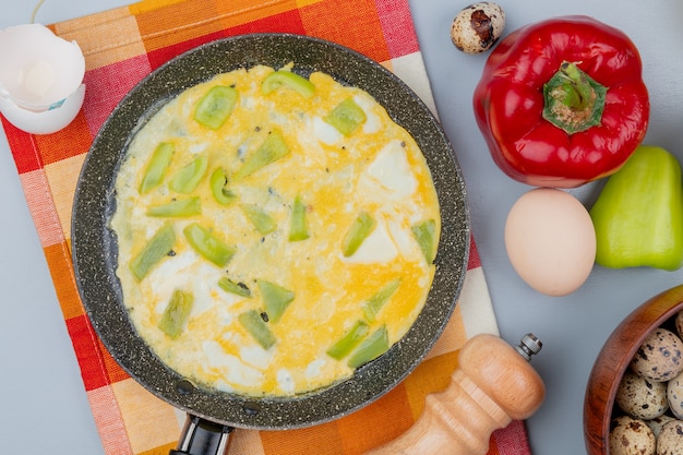 Top view of fried egg on a frying pan with colorful peppers with quail eggs on a wooden bowl on white background