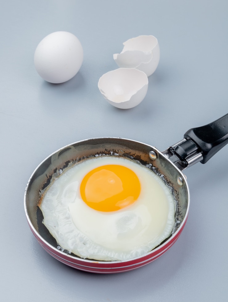 無料Photo 白い背景の上のひびの入った卵の殻を持つフライパンで目玉焼きのトップビュー
