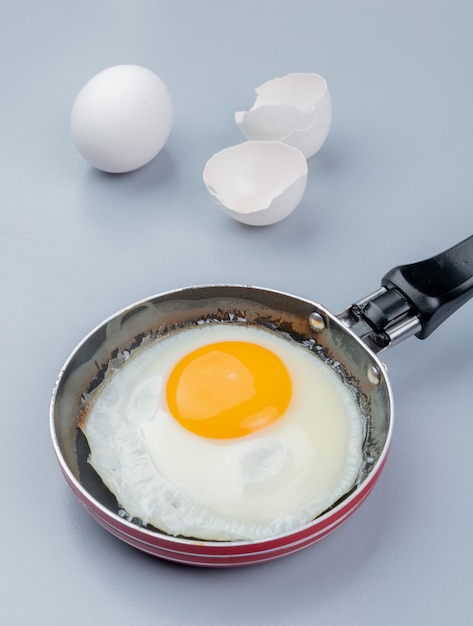 Top view of fried egg on a frying pan with cracked egg shell on white background