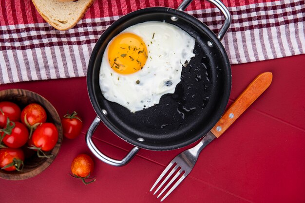 赤のチェック柄の布とトマトとフォークのボウルにパンとフライパンで卵焼きの平面図