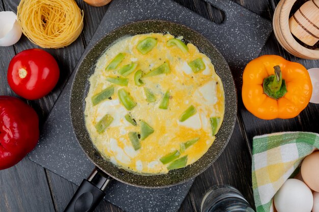 Top view of fried egg on a pan with colorful bell peppers with a tomato on a wooden background