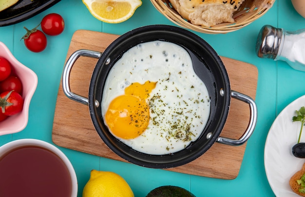 Free photo top view of fried egg on pan on wood kitchen board with lemonnd a bucket of breads on blue