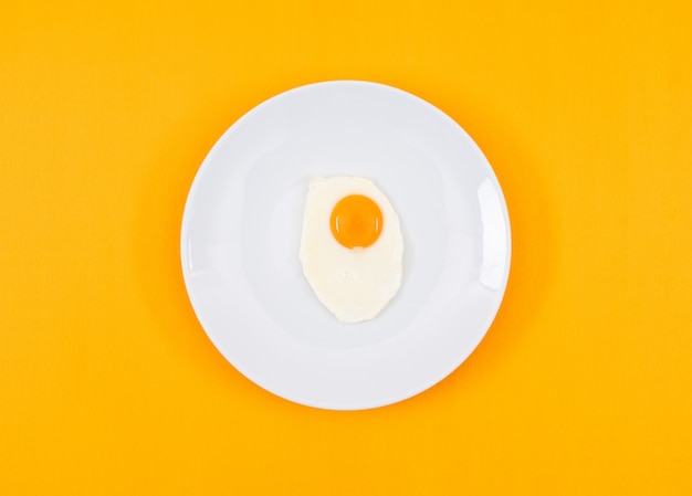 Top view of fried egg on white plate and on yellow surface horizontal