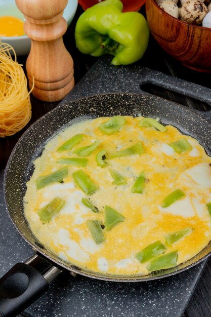 Top view of fried egg with green bell pepper on a pan with fresh bell pepper with quail eggs on a wooden background on black background