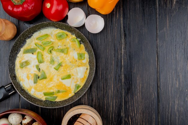 Top view of fried egg with slices of green bell pepper on a frying pan on a wooden background with copy space