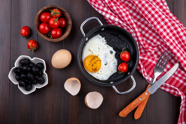 격자 무늬 천에 칼로 냄비에 토마토와 포크와 껍질과 나무에 토마토와 올리브의 그릇에 계란의 상위 뷰