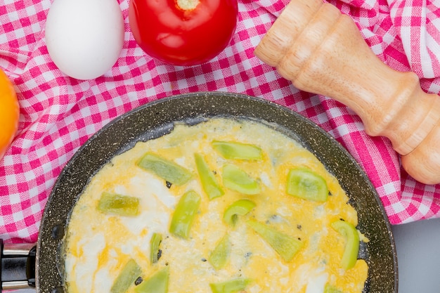 Vista superiore delle uova fritte su una padella con le fette verdi del peperone dolce su un panno controllato su un fondo bianco