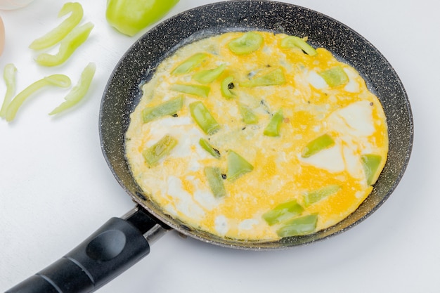 Вид сверху яичницы на сковороде с кусочками зеленого перца на белом фоне