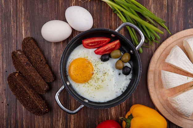 토마토와 올리브와 녹색 양파 검은 빵과 나무 배경에 죽은 태아의 치즈와 프라이팬에 상위 뷰 튀긴 계란